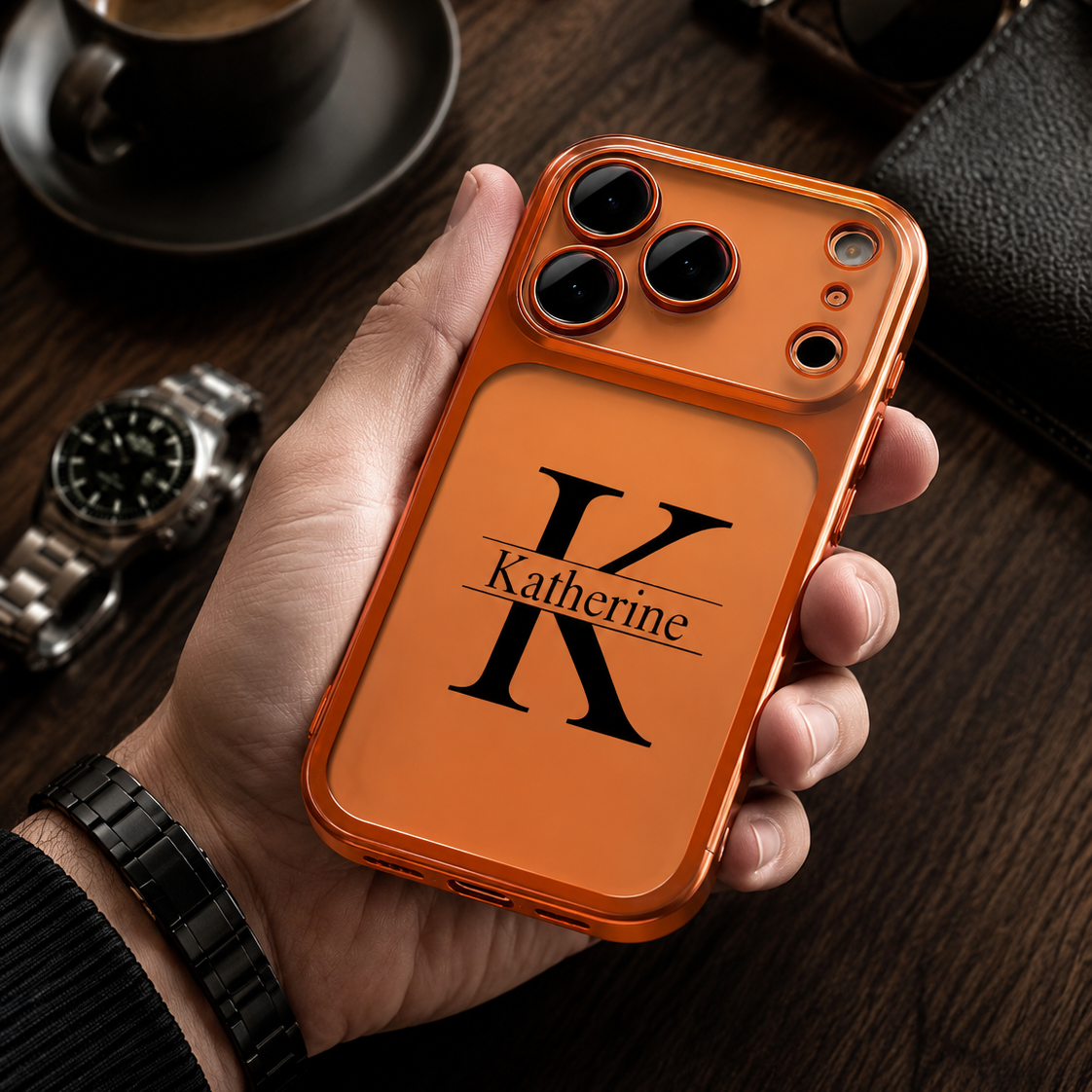 Hand holding an orange phone case with 'Katherine' branding on a wooden surface.